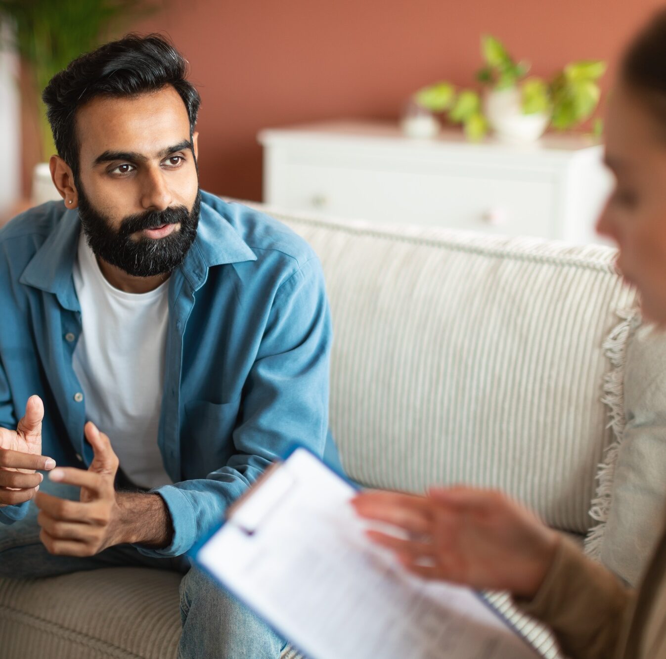 Young Indian man consulting with professional psychologist sitting indoor